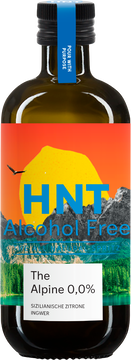 Im Bild ist eine braune Glasflasche mit Schraubverschluss zu sehen, die ein sehr farbenfrohes, künstlerisches Etikett mit einer Alpenlandschaft zeigt, in der eine große Zitrone die Sonne ersetzt. Auf dem Etikett stehen die Worte „HNT Alcohol Free“ in großen blauen Buchstaben, und darunter steht in einem weißen Feld „The Alpine 0,0%“ sowie die Geschmacksrichtung „Sizilianische Zitrone und Ingwer