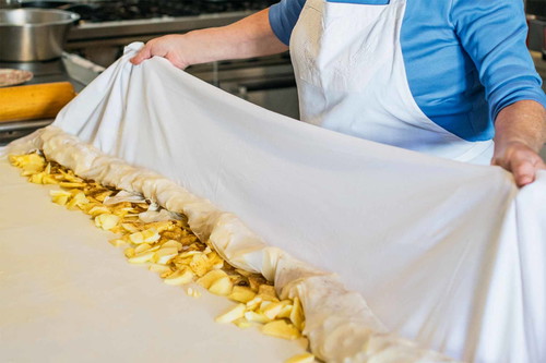 10. Einrollen: Die breiten Enden des Strudelteigs darüberschlagen und dann das überhängende Ende auf die Äpfel legen.