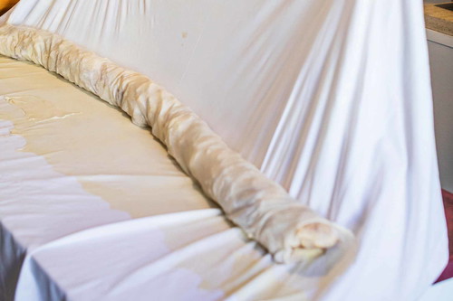 Mithilfe des Leintuchs den ganzen Strudel um die eigene Achse rollen lassen, sodass eine lange Rolle entsteht.