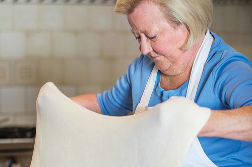 6. Strudel ziehen: Vorsichtig in die Hand nehmen, sodass der Teig auf den Handrücken beider Hände zu liegen kommt. Mit beiden Handrücken auseinanderziehen, dabei leicht schütteln und schupfen, sodass der Teig sich gleichmäßig auseinanderziehen lässt.