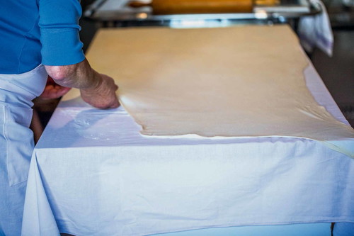 7. Teig ausziehen: Den Teig wieder auf das Leintuch legen und an den Rändern sachte auseinanderziehen, sodass der Teig hauchdünn über den ganzen Tisch gebreitet wird.