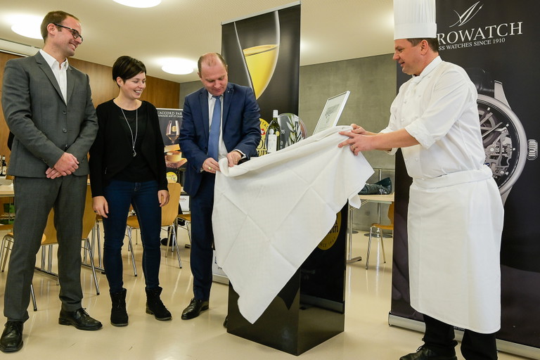 Philippe Leuba und Frank Giovannini enthüllen den Siegerwein. Links Philippe Meyer, Chef der Kantonsdomänen, und Marjorie Bonvin, Kellermeisterin bei Badoux, die den Villeneuve vinifiziert hatte.