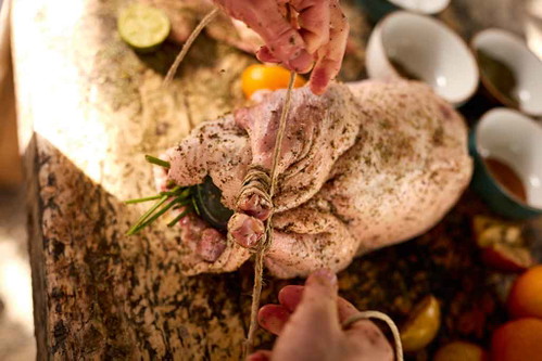 4. Danach reibt er den Braten mit Gewürzen (Salz und Majoran) ein und bindet ihn an den Keulen mit einem Küchengarn zusammen.