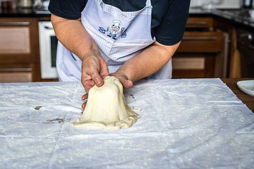 5. Strudelteig ziehen. Von der Mitte beginnend vorsichtig in alle Richtungen ziehen.