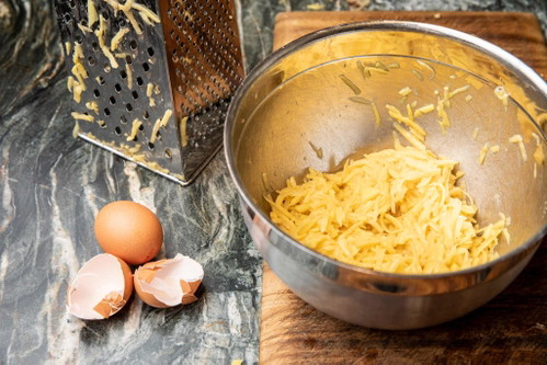 Für den Erdäpfelpuffer geriebene Erdäpfel mit dem Ei, Zwiebel und Gewürzen vermengen.