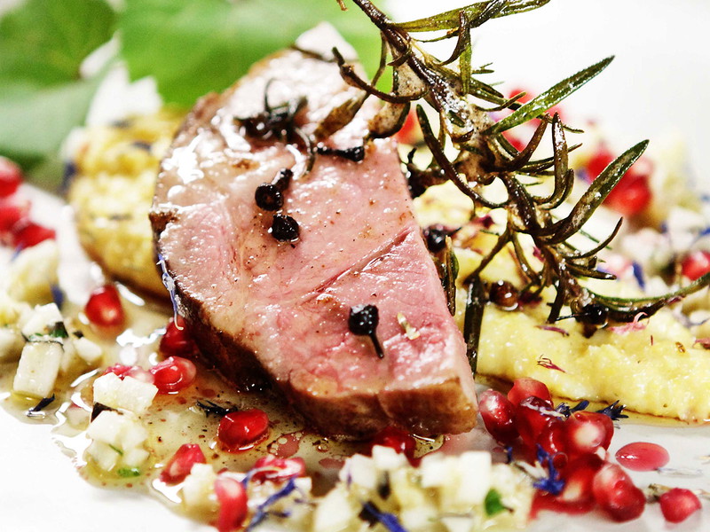 Ein rosa Schweineschopf mit cremiger Polenta und Granatapfelkernen.