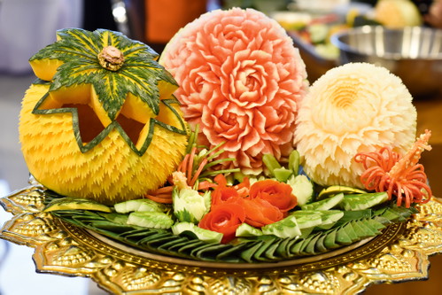 Präsentation ist die halbe Miete – das wissen auch die Köche Thailands längst. So liegt ein Hauptaugenmerk in der thailändischen Küche traditionell auf der Optik der Gerichte. Die sind mit ihren vielen frischen Zutaten und deren kraftvollen Farben – von Chilirot bis Basilikumgrün – zwar meist ohnehin sehr hübsch anzusehen. Zusätzlich wird aber oft noch mit verspielter und meist auch besonders aufwendiger Dekoration gearbeitet. Was man früher Tournieren nannte, heißt heute Food Carving: das kunstvolle Schnitzen von grafischen Mustern oder Figuren, vornehmlich aus Obst und Gemüse. Gerade in der gehobeneren thailändischen Gastronomie sind dabei oftmals wahre Meister am Werk.