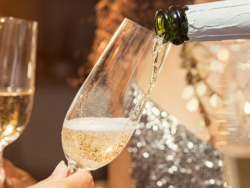 Hand pouring champagne from bottle into glasses with friends around him. Closeup of hand pouring white wine in flutes during party. Detail shot of new yearâ€™s eve celebration.