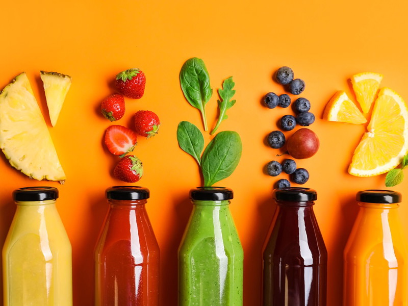 Flat lay composition with bottles of delicious juices and fresh ingredients on orange background