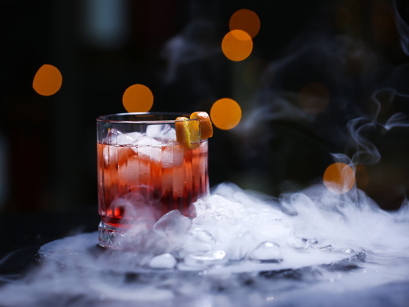 Glass of tasty Negroni cocktail and ice cubes on table against blurred background