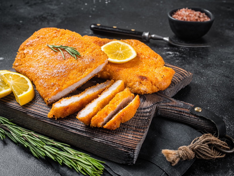 Fried sliced weiner schnitzel on a wooden board with herbs. Black background. Top view
