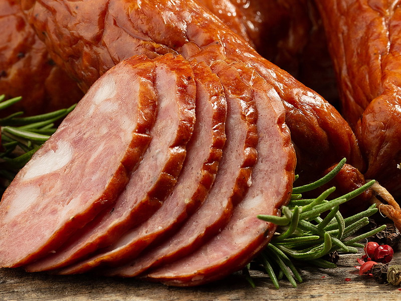Sliced kielbasa with vegetables on wooden background.