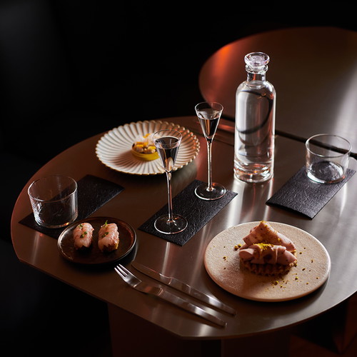 Der »Oud- und Santal-Martini«, ein »Walnussleder-Negroni« sowie ein »Gaumenreiniger« aus Neroli und Petitgrain-Tee. Dazu werden Snacks aus Palamós-Garnelenkroketten, Manchego-Waffel, Trüffel, Mortadella und Pistazie sowie gedämpften Herzmuscheln mit grünem Apfel und Yuzu gereicht.
