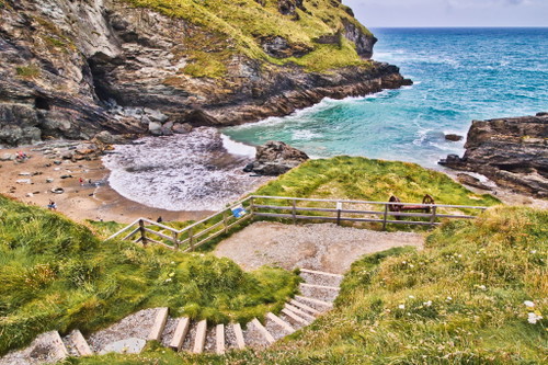 Panoramablick auf die Küste mit einem Sandstrand, umgeben von Felsklippen und üppigem Grün. In Tintagel, Cornwall, Großbritannien.