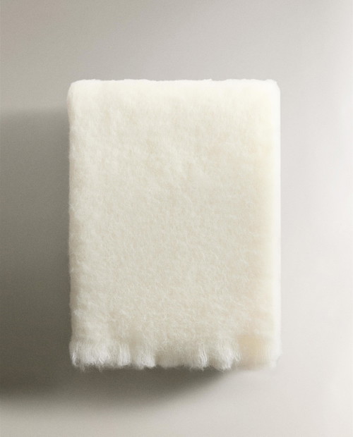 La coperta bianca in lana mohair tinta unita, con piccole frange, per avvolgersi sul divano in un caldo abbraccio.
