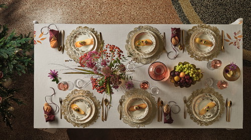 La tavola si fa teatro di eleganza e convivialità, con piatti in porcellana decorati color oro e sottopiatti di diverse fantasie.
