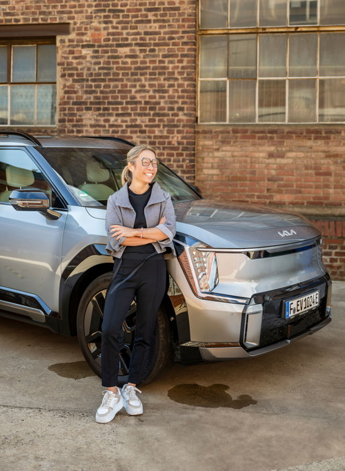Spitzenköchin und Kia-Markenbotschafterin Sarah Henke mit ihrem vollelektrischen Kia EV9. Neben reichlich Stauraum für den Großeinkauf wird er dank Vehicle-to-Load-Funktion (V2L) zur mobilen Stromquelle – ideal, um den Elektrogrill für das erste Angrillen im Grünen ganz einfach anzuschließen.