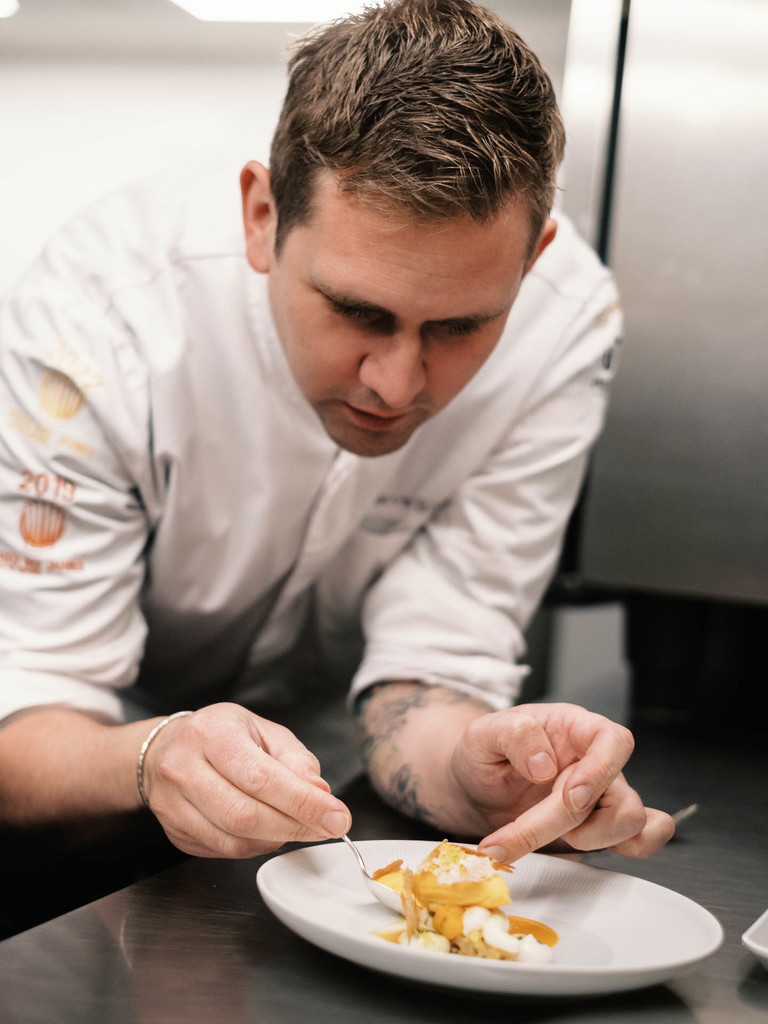 Der staatlich geprüfte Gastronom und Küchenmeister steht für eine präzise, produktfokussierte Küche mit klarer regionaler Handschrift und modernen internationalen Einflüssen. Marvin Böhms kulinarische Laufbahn begann in der »Schwarzwaldstube« der »Traube Tonbach« bei Harald Wohlfahrt. Prägend war seine Station im Drei-Sterne-Restaurant »Aqua« im »The Ritz-Carlton« Wolfsburg, wo er von 2010 bis 2024 unter Sven Elverfeld tätig war.
Parallel dazu etablierte sich Böhm als einer der erfolgreichsten deutschen Wettbewerbsköche: Er gewann dreimal den Bocuse d’Or Deutschland (2016, 2018, 2023) und vertrat Deutschland mehrfach auf internationaler Ebene, unter anderem im Weltfinale in Lyon.