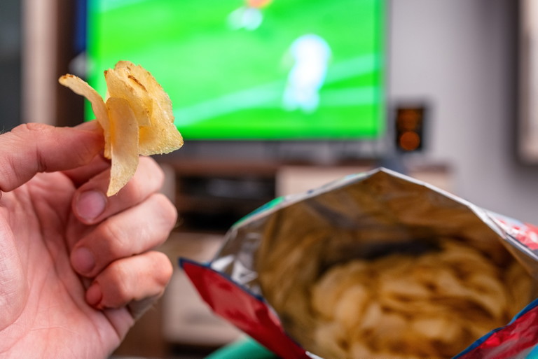 Eine Chipstüte auf der Couch: Gerade beim Fernsehen essen viele unbewusst mehr, als sie eigentlich vorhatten.