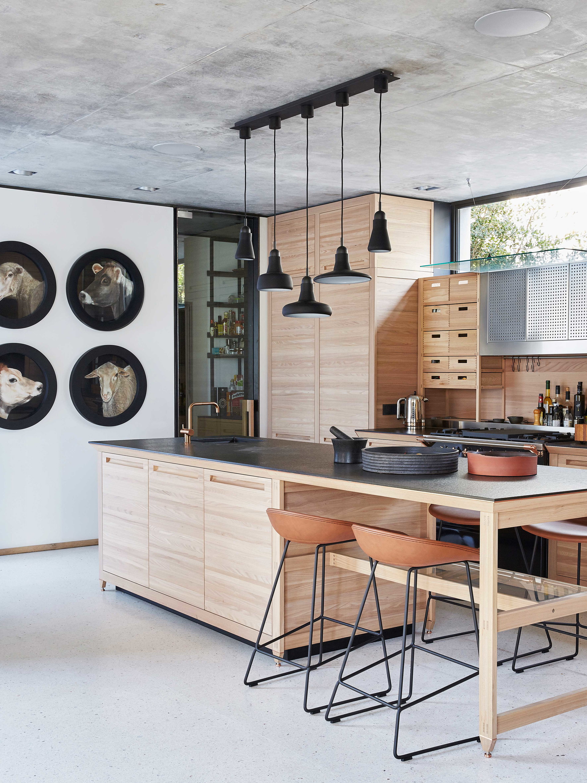 Scandi Noir: Gelassen vereint diese Küche geradliniges Holz mit Akzenten aus chicem Schwarz (z. B. die Hängeleuchten von Brokis), die Orientierung im Raum bieten und ihn mit einer urbanen Raffinesse ausstatten. Die Küchenkästen von Valcucine sind aus nachhaltigem Ulmenholz, die Arbeitsflächen aus Granit. Anflüge von Wärme wehen in Form gebürsteter Kupferakzente von Ofen, Armatur und den mit hell­braunem Leder gepolsterten Hockern von Hay her.
