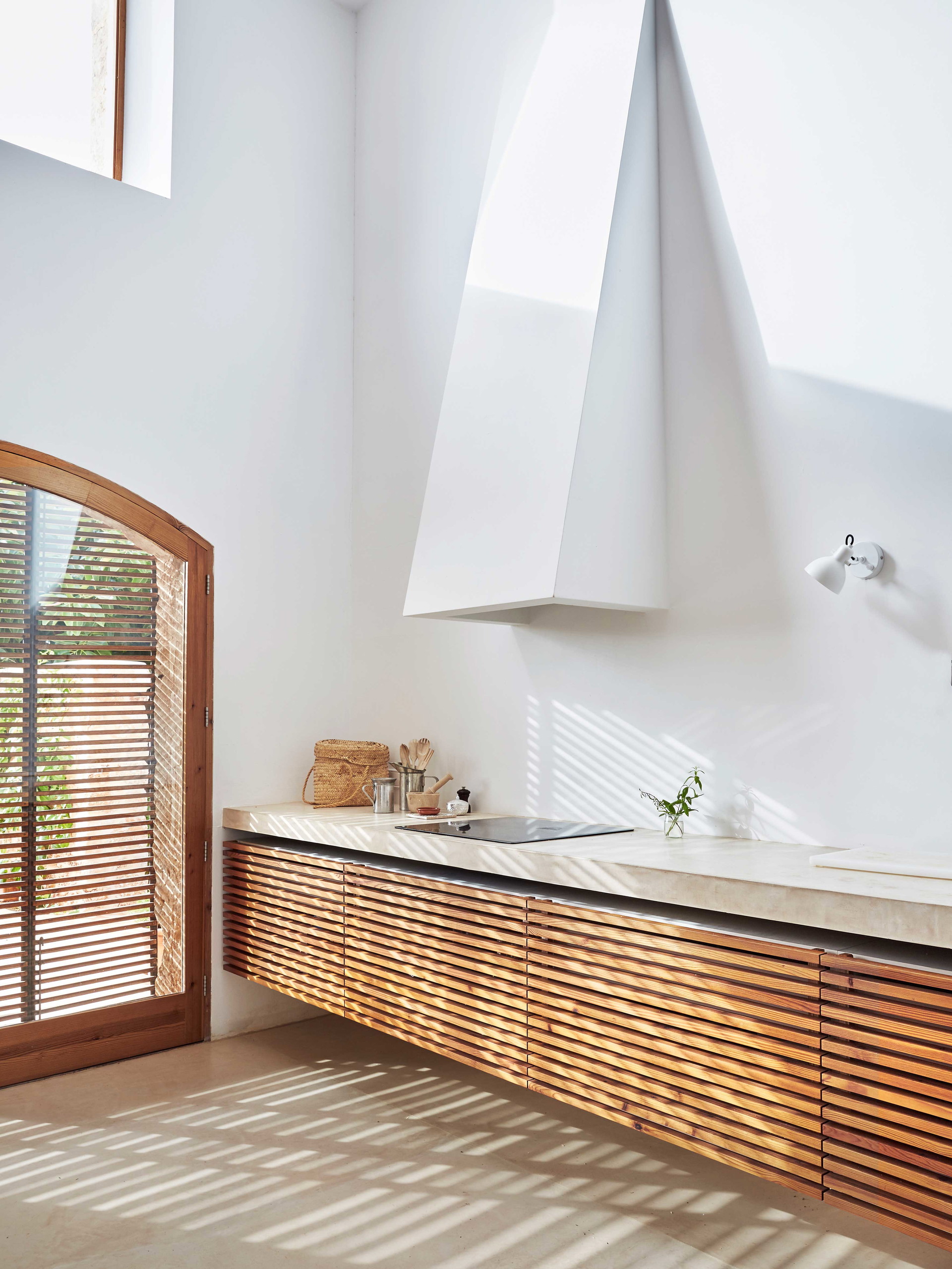 Balanceakt: Holz ist der Star dieser poetischen Interpretation von architektonischem Minimalismus. Als einziger natürlicher Baustoff inmitten von Gips, Glas und Beton gibt Holz Struktur und Wärme. Die Lamellenoptik der Fronten greift die Struktur der Außenrollos auf und gibt dem Raum visuelle Energie. Praktische Notwendigkeiten werden auf ihre Essenz reduziert, technisch steht die Induktionsplatte von Smeg im Mittelpunkt, auf sonstige Geräte wird verzichtet. Die schwebenden Küchenkästen sowie die eingelassenen Elemente verleihen ein Gefühl der Schwerelosigkeit.
