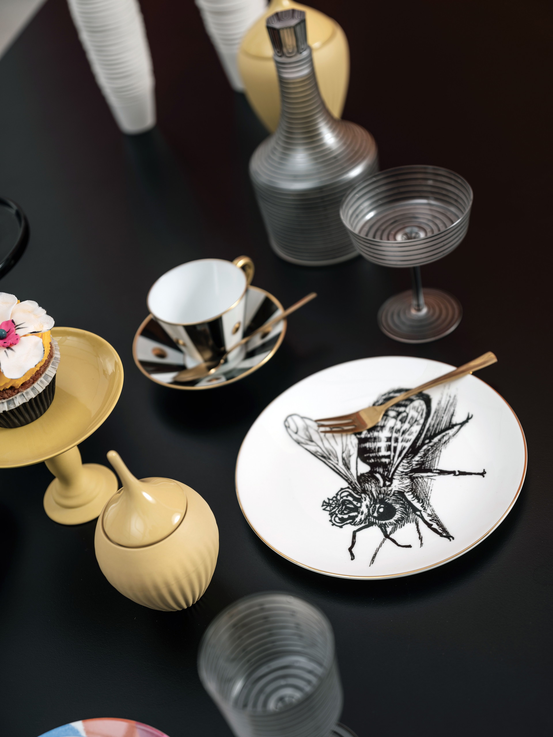 Senfgelbe Etagère und Dose von Feine Dinge. feinedinge.at; Teller »Queen Bee« von Rory Dobner via Ma Maison. ma-maison.at;&nbsp;Besteck von Zara Home. zarahome.com; Tasse und Untertasse von Bernardaud Lipari via Cuisinarum. cuisinarum.at; Champagner-Schale »Hoffmann« von Lobmeyr. lobmeyr.at;&nbsp;Cupcake von Cupcakes Manufaktur Wien. cupcakes-manufaktur.at