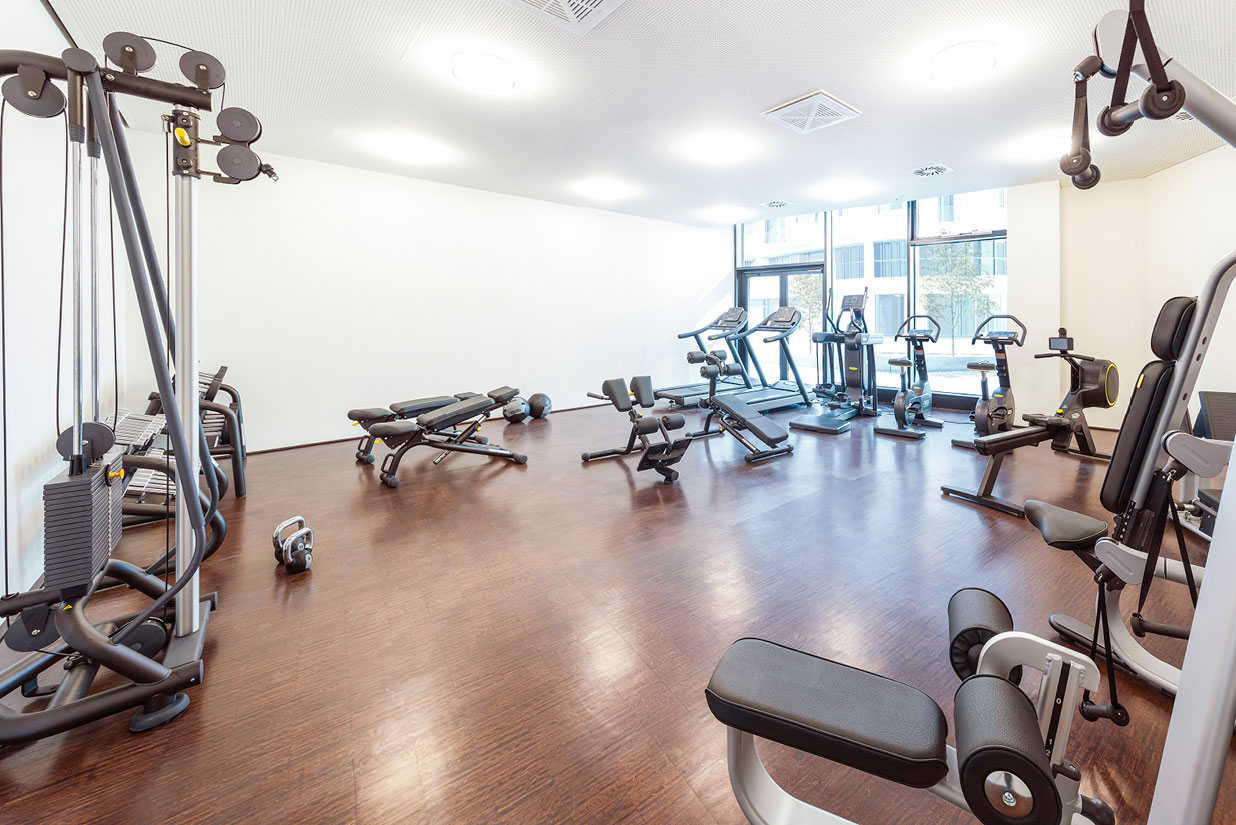 Attraktiver Fitnessraum mit Technogym®-Geräten und Blick auf die begrünte Plaza.