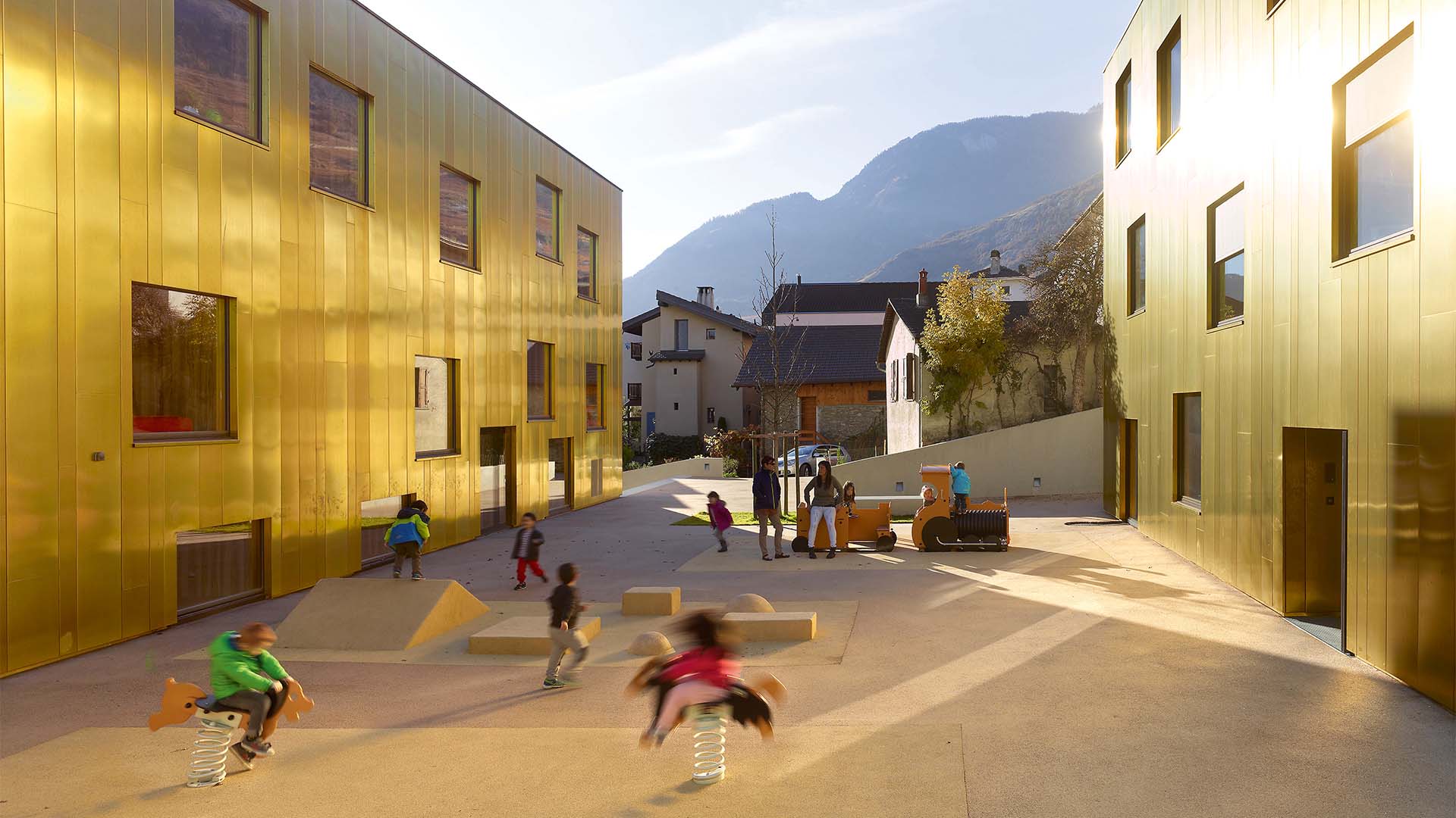 Zwischen Genfer See und Matterhorn liegt diese edle Schule,&nbsp;die die Savioz Fabrizzi Architectes im Jahr 2015 in die Landschaft setzten. Eines der beiden Gebäude beherbergt Kinderkrippe und Kindergarten, im anderen Haus befinden sich Schule und Hort. Die goldene, stark spiegelnde Fassade übernimmt bei diesem Projekt weniger die Rolle einer edlen&nbsp;Schatulle als vielmehr&nbsp;die Aufgabe, mit Spiegelbildern, reflektierenden Farben und&nbsp;wild&nbsp;positionierten Fenstern Spiel und Spaß ins mitunter raue Gebirgsklima zu zaubern. sf-ar.ch, vetroz.ch