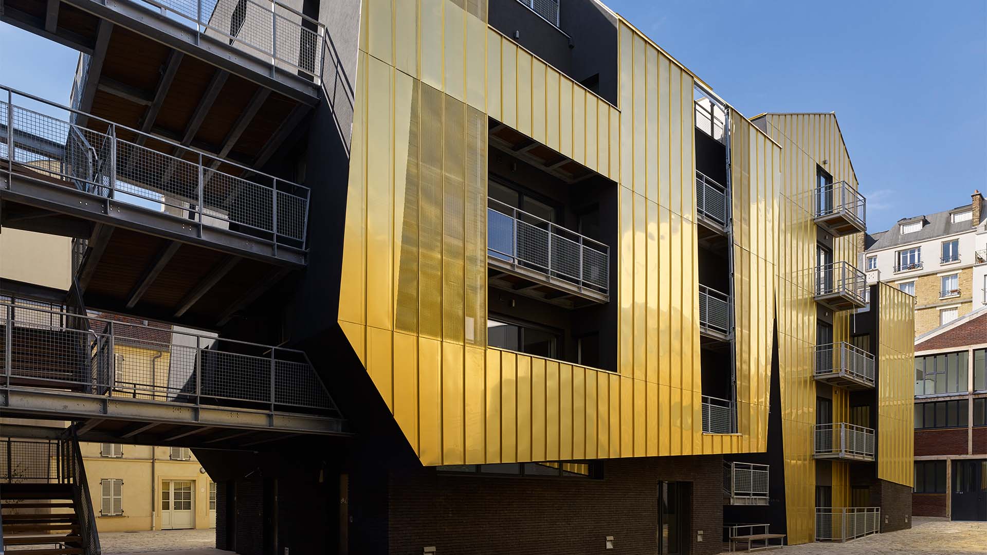 In der Rue de Crimée im 19.&nbsp;Arrondissement von Paris hat sich das Büro Metek Architecture&nbsp;etwas Besonderes einfallen lassen&nbsp;– und hüllte diesen sozialen Wohnbau mit 31&nbsp;geförderten&nbsp;Wohnungen und sieben Kunstateliers in eine Blechfassade aus goldglänzenden&nbsp;Stehfalzplatten. Dank dem stark reflektierenden Metall&nbsp;– einer Kupfer-Aluminium-Legierung,&nbsp;die über Dach und Fassaden gezogen wird und das Bauwerk in eine monolithische Skulptur&nbsp;verwandelt&nbsp;– gelangt mehr Sonnenlicht in die Enge des Pariser Hinterhofs. ​​​​​​​metek-architecture.com​​​​​​​