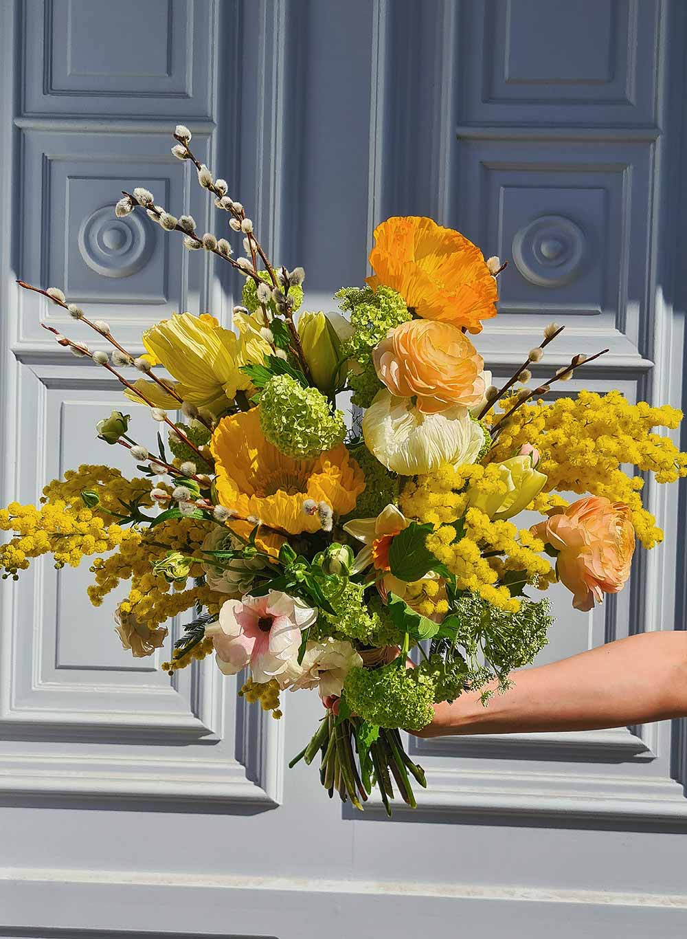 Man muss das Rad nicht neu erfinden, Ranunkel wurden auch beim Strauß von Blumen Doll verarbeitet. Dafür kommt Mohn dazu und ​​Mimosen, die sich herrlich an die Palmkatzerl schmiegen. dollsblumen.at