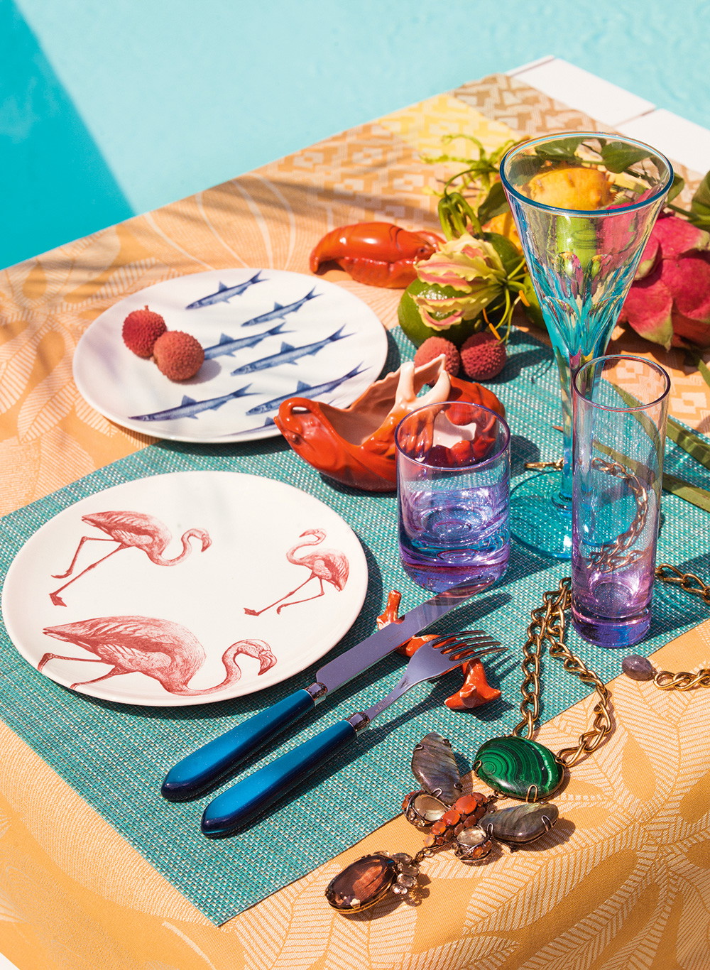Besteck von Capdeco via Ma Maison.&nbsp; Tischdecke Le Jacquard Français via Cuisinarum.&nbsp; Tischset von Chilewich via Cuisinarium. &nbsp; Glasbecher aus Alexandritglas Italien um 1970, und türkise Glasflöten mit Schälschliff Böhmen um 1940, via Schwab &amp; Patzl Kunsthandel. Teller mit Flamingos »Flore &amp; Faune« via Albin Denk. Kette aus Malachit, Labrador, Karneol und Catrin by Iradj, NY 2010, via Schwab &amp; Patzl Kunsthandel.