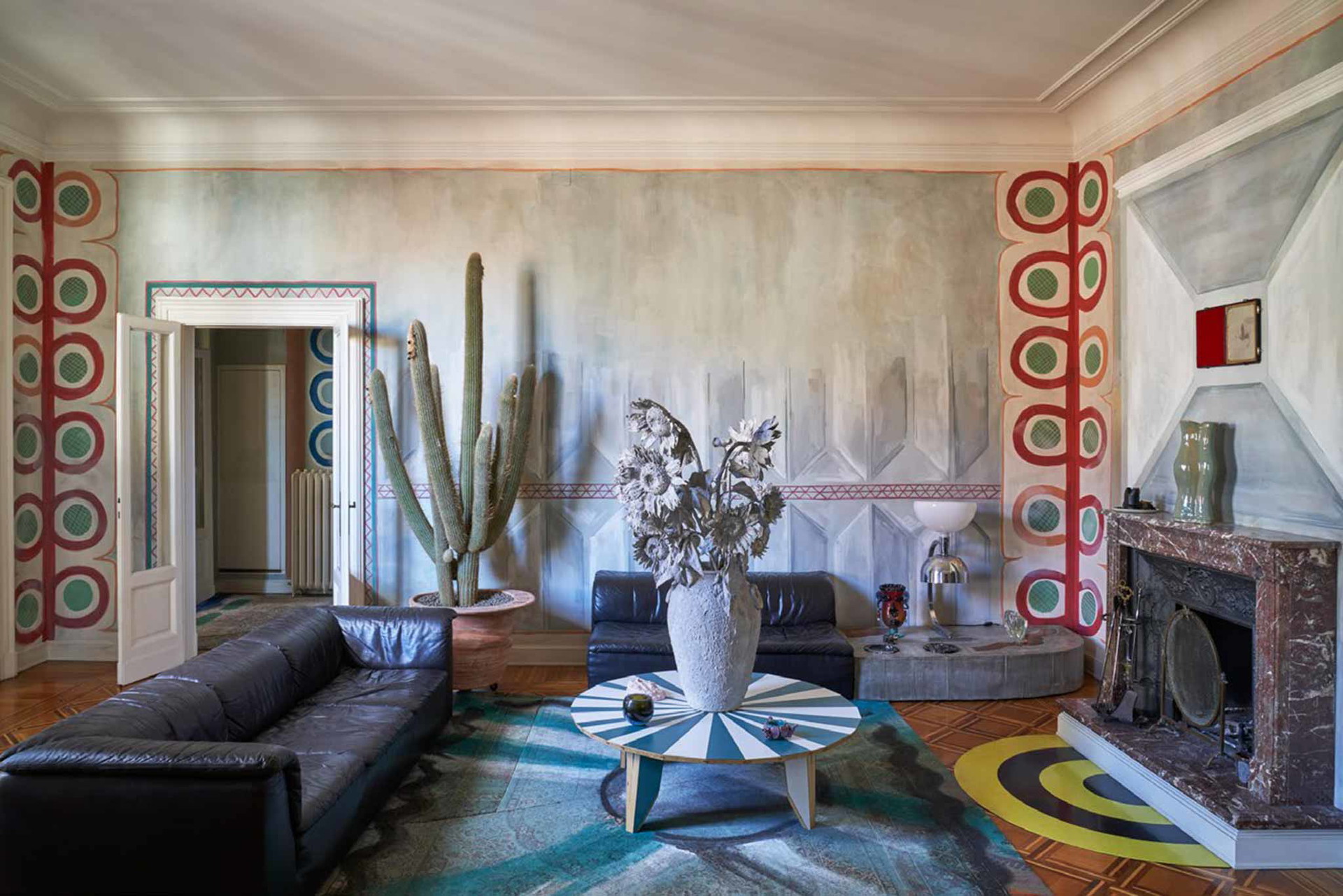 Feuerstelle Der Kaktus von Flores verleiht dem Wohnzimmer eine besondere Note. Die Zementvase von Mario Torre steht auf einem Couchtisch von Martino Gamper. Die Lampe aus Chrom und Weißglas stammt von Franco Albini. Das Kaminsims schmückt eine Vase von Hylton Nel. Darüber hängt ein Bild von Mat Collishaw.