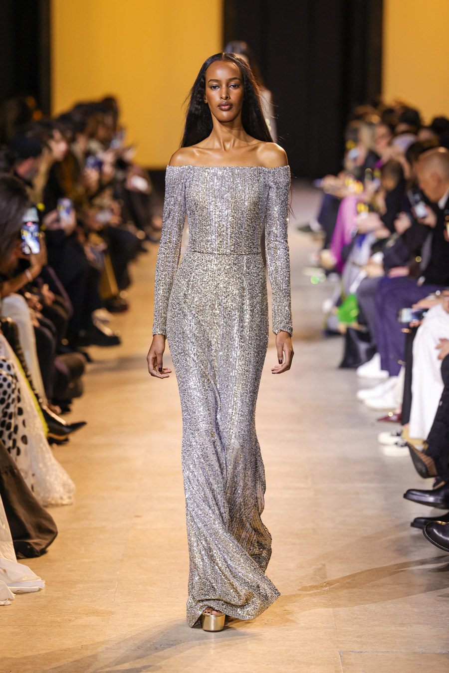 Graceland-Glam: In pure Eleganz gehüllt: Das bodenlange ­schulterfreie Kleid der 
HW24-Kollektion 
funkelt in zig Pailletten, die in gold-silbernen Kaskaden über das 
Design verlaufen. 
eliesaab.com