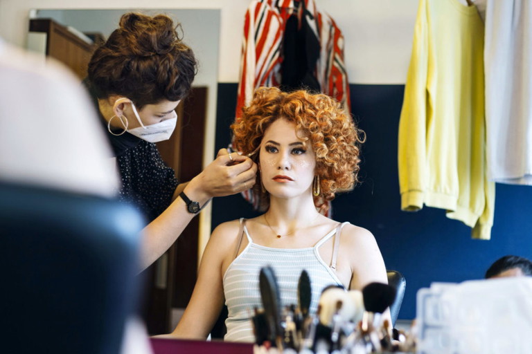 In der Maske wird aus Lisa Habermann, die glatte, braune Haare trägt, durch eine auffällige Perücke ein lockiger Rotschopf.