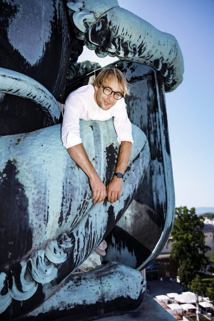 Mirco Kreibich entspannt sich am heraldischen Löwen auf dem Haus für Mozart in Salzburg. Direkt unter ihm der Max-Reinhardt-Platz.