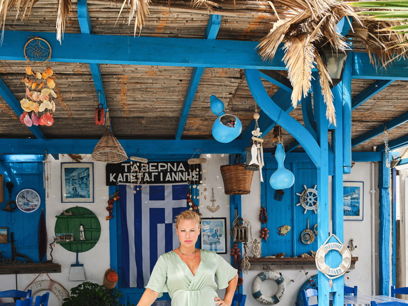 Eine Taverne, blaue Fensterläden, die griechische Fahne, getrocknete Oreganobüschel an den Wänden. Davor Katharina Straßer. Den Gehstock hat sie sich ausgeborgt. Herzlich willkommen, hier sehen Sie den Urlaubsort der Schauspielerin. Wo er genau ist? Auf einer griechischen Insel. Ihr Name wird nicht verraten, sorry.