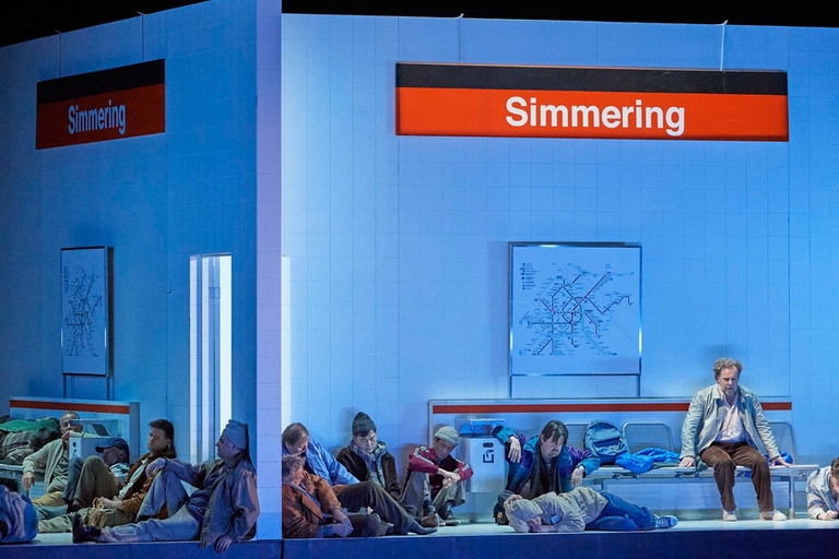 Eine Gruppe von Personen sitzt auf dem Boden in einer U-Bahn-Station mit dem Schild "Simmering" im Hintergrund.